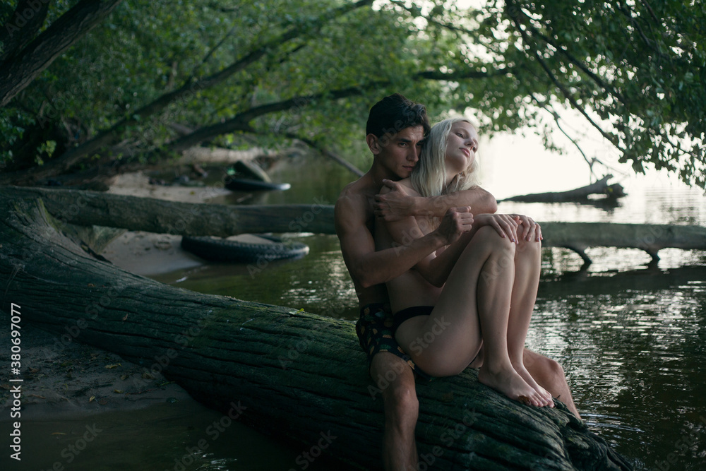 a girl and a guy hug and sit on a tree trunk on a river beach a girl and a guy hug and sit on a tree trunk on a river beach