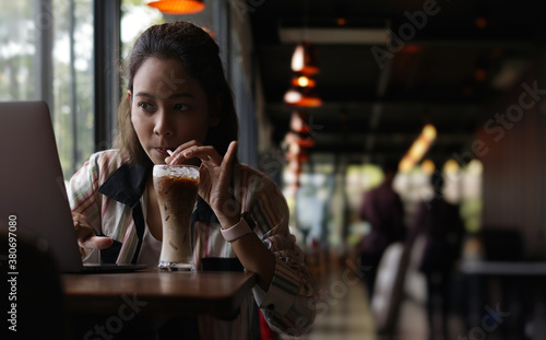 Portrait of young aisian female drinking ice coffee and thoughtfully looking out of the coffee shop window while enjoying her leisure time alone,social distancing concept. © greenbutterfly