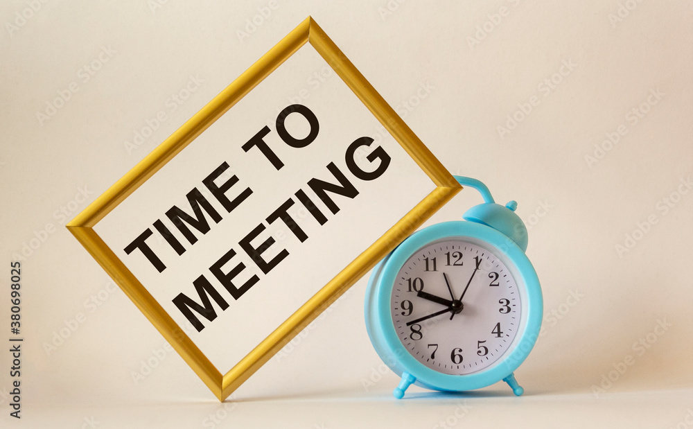 Time for a meeting, the text is written on a gold frame, next to an alarm clock on a white background Time for a meeting, the text is written on a gold frame, next to an alarm clock on a white background