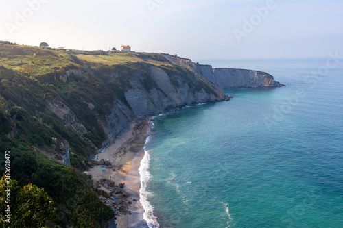 Beach and cliffs by the ocean at sunset. Small house on top of the hill at sunset time. Hidden beach at the botton of a cliff. Green grass on top of the rocks. Playa de Serín, Asturias, North of Spain