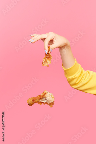 Woman dangles bitten fried chicken drumstick as it falls through the air photo