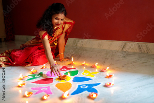 Indian woman lighting oil lamps during diwali and decorating with rangoli