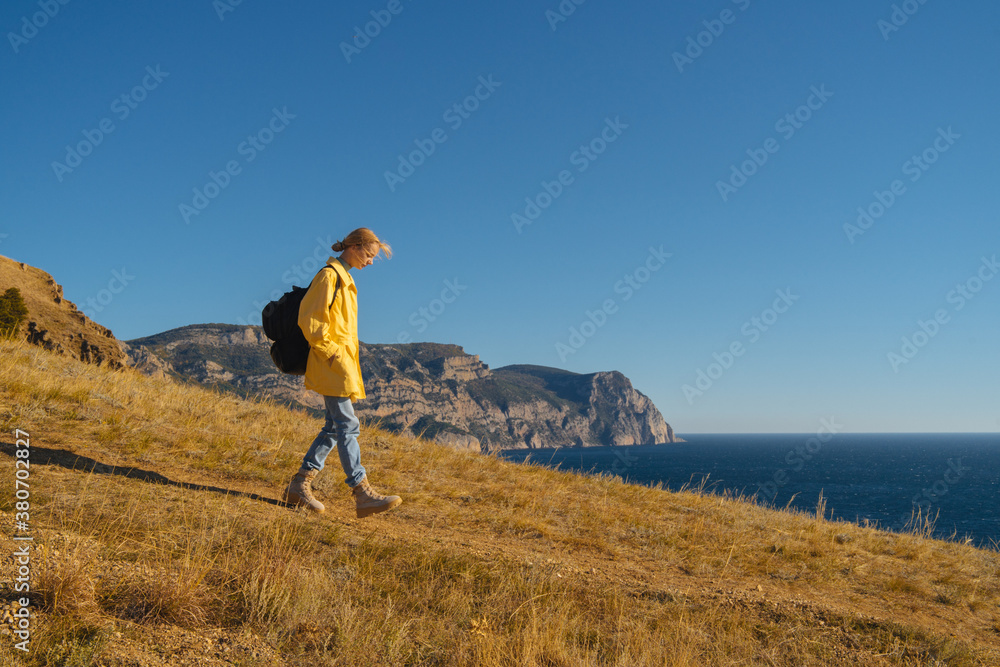 blonde in tourist clothes walks along the slope covered with yellow grass blonde in tourist clothes walks along the slope covered with yellow grass