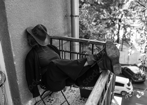 The girl is sitting on the balcony, the female is hiding behind a hat. Depressive and withdrawn mood