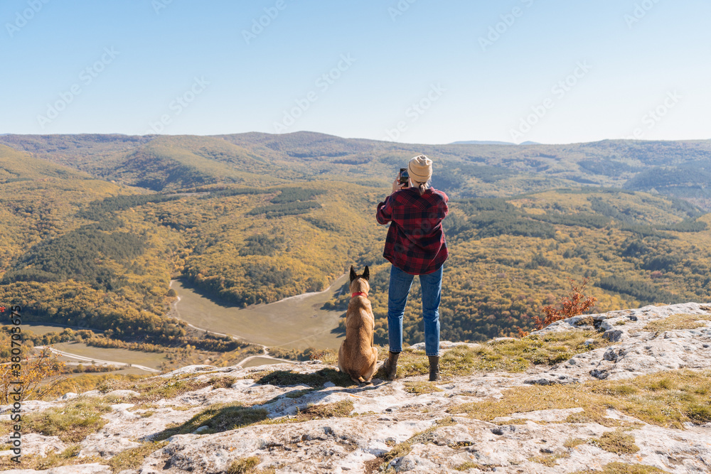 A girl photographs a wonderful landscape on the phone while her dog sits nearby A girl photographs a wonderful landscape on the phone while her dog sits nearby