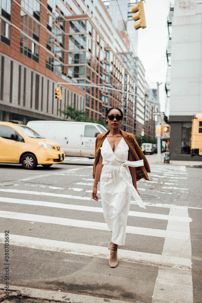 Woman in white dress and tan coat walking across the street Woman in white dress and tan coat walking across the street