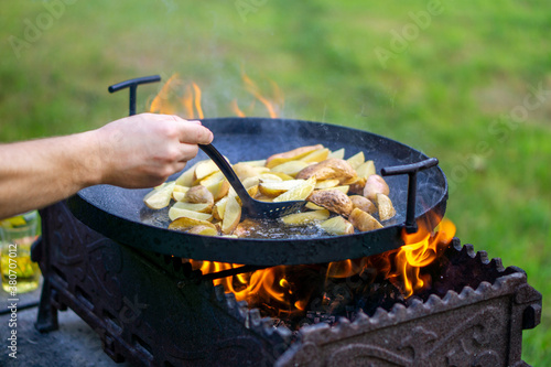 the cook stirs the potatoes which are fried on an open fire in oil, copy space. out of doors