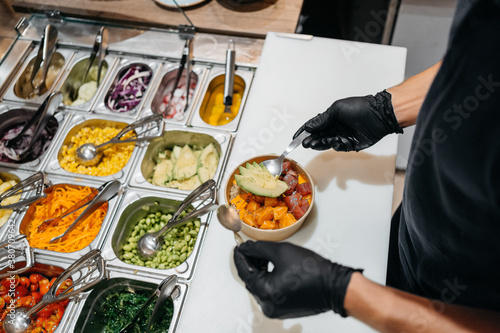 Anonymous waiter filling a poke bowl with food