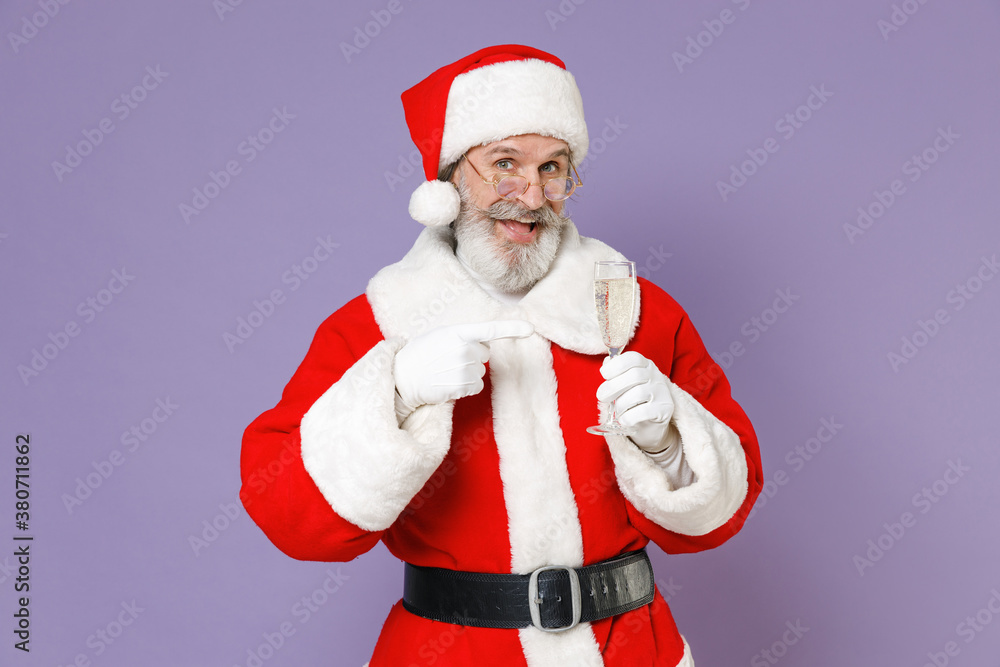 Excited Santa Claus man in Christmas hat red suit coat gloves glasses point index finger on glass of champagne isolated on violet background studio. Happy New Year celebration merry holiday concept. Excited Santa Claus man in Christmas hat red suit coat gloves glasses point index finger on glass of champagne isolated on violet background studio. Happy New Year celebration merry holiday concept.