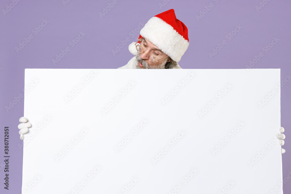 Shocked amazed Santa Claus man in Christmas hat red coat gloves glasses hold big white empty blank billboard isolated on violet background studio. Happy New Year celebration merry holiday concept. Shocked amazed Santa Claus man in Christmas hat red coat gloves glasses hold big white empty blank billboard isolated on violet background studio. Happy New Year celebration merry holiday concept.