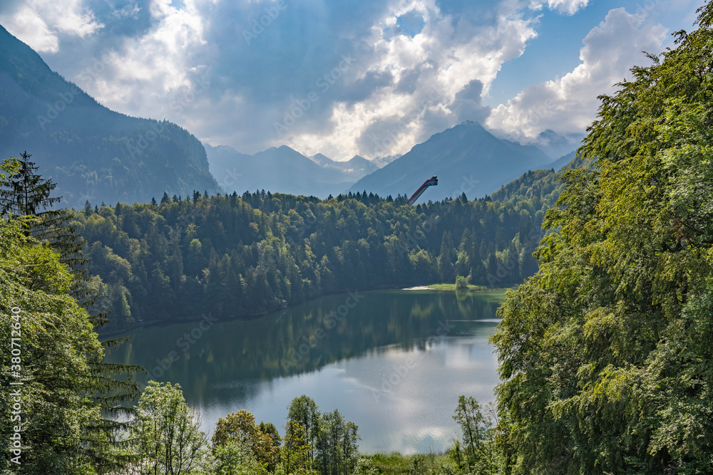 nice senior woman riding her electric mountain bike above the Freiberg Lake and a big ski flying hill in the Allgau Alps near Oberstdorf, Bavaria, Germany
