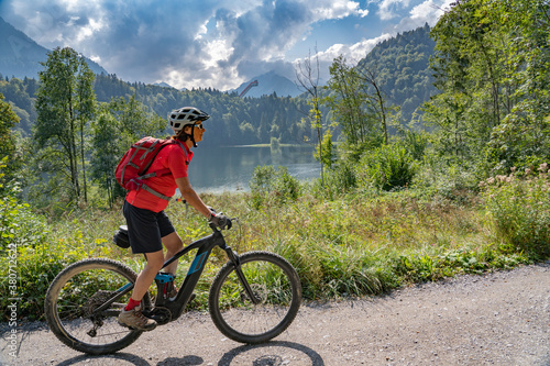 nice senior woman riding her electric mountain bike above the Freiberg Lake and a big ski flying hill in the Allgau Alps near Oberstdorf, Bavaria, Germany 