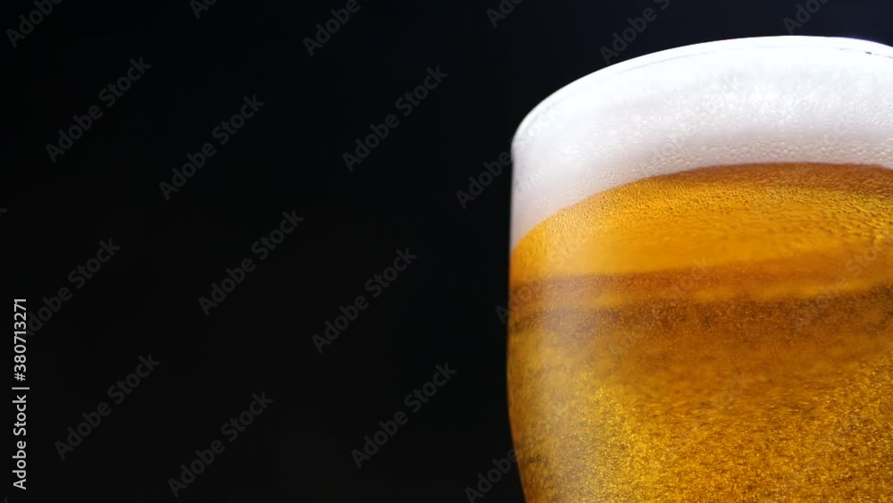 Pan right view of glass cup of bubbling fresh beer with foam placed in thin fume on dark blue background
