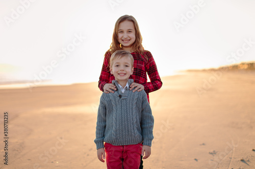 Big sister standing behind her younger brother on a beach photo