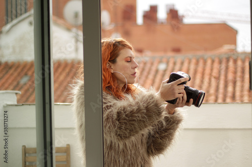 mujer de cabello naranja en exteriores haciendo una fotografía con cámara profesional y un abrigo de pelos gris
