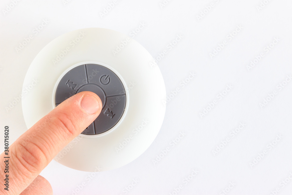 White circle mini speaker on isolated white background with copy space. Man finger is pressing play button. White circle mini speaker on isolated white background with copy space. Man finger is pressing play button.
