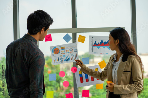 Mixed race business woman standing and presenting business project on clear board with male colleague.