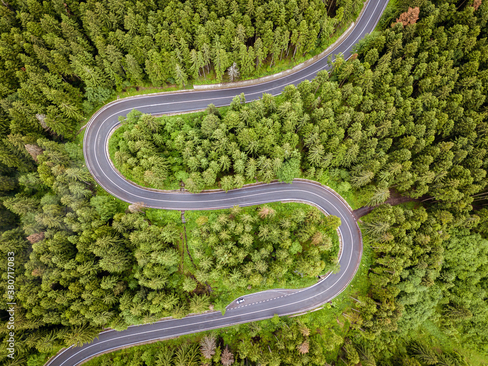 A winding road visible from the air, between green forests