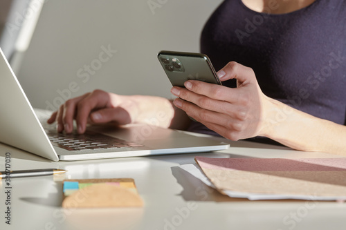 Woman interacting with smartphone while using laptop in contempo photo