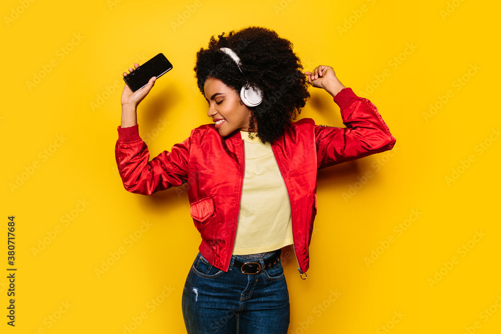 Beautiful afro woman listening to music with white headphones and cellphone