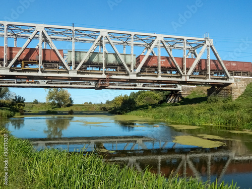 a freight train travels on a metal railway bridge, reflections in the river 