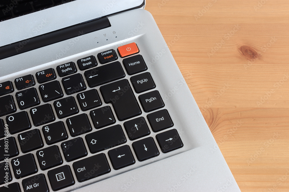 Cropped top view of modern grey laptop with orange shut down button on the light brown wooden table Cropped top view of modern grey laptop with orange shut down button on the light brown wooden table