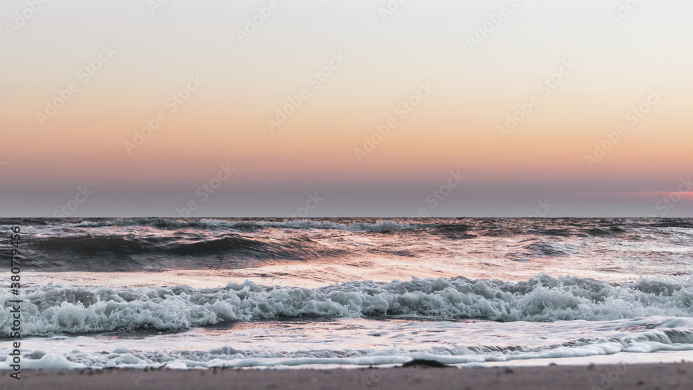 Sunset sky with stormy white glossy waves on sea shore sand beach in pastel colors