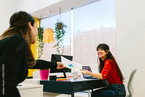 Smiling women passing paper to each other photo