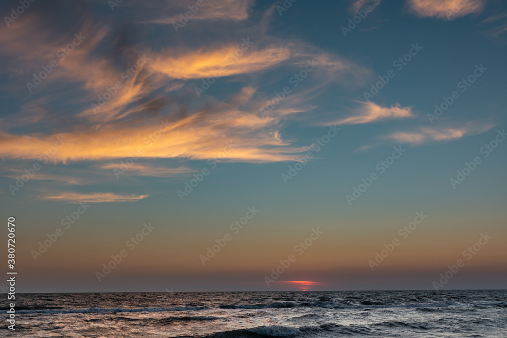 Sunset sun down hidden on horizon with stormy waves sea shore and epic colorful clouds lightened by warm sun