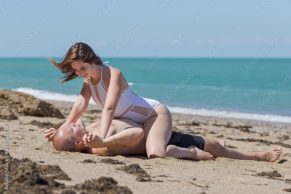 Young woman in white swimwear sits astride her bare-chested man and holds his hands