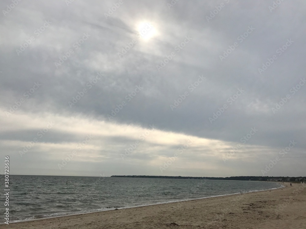 A cloudy sky on the ocean with the sun peeking through, 