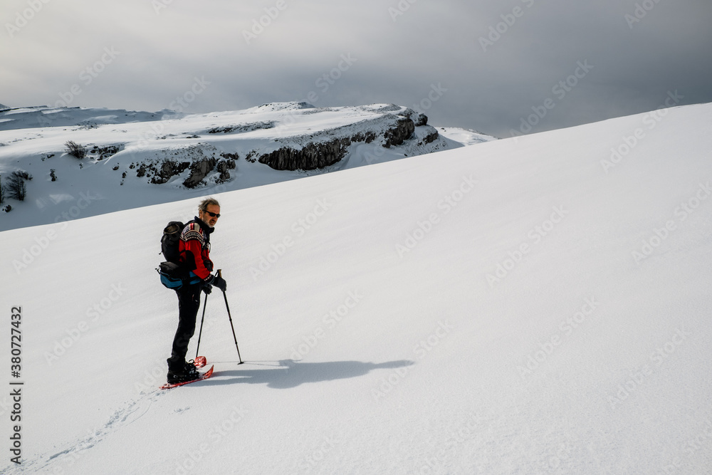 A senior man is walking a pristine mountain with snowshoes A senior man is walking a pristine mountain with snowshoes