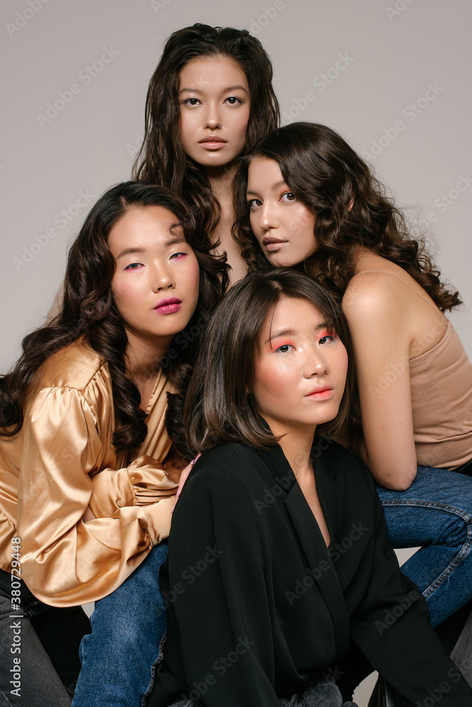 Multicultural shinning girls are sitting together on the grey background Multicultural shinning girls are sitting together on the grey background