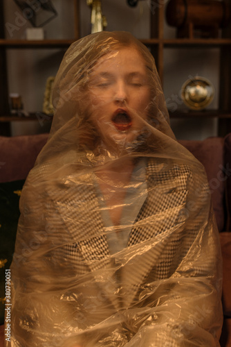Portrait of a girl in a plastic bag choking in a room