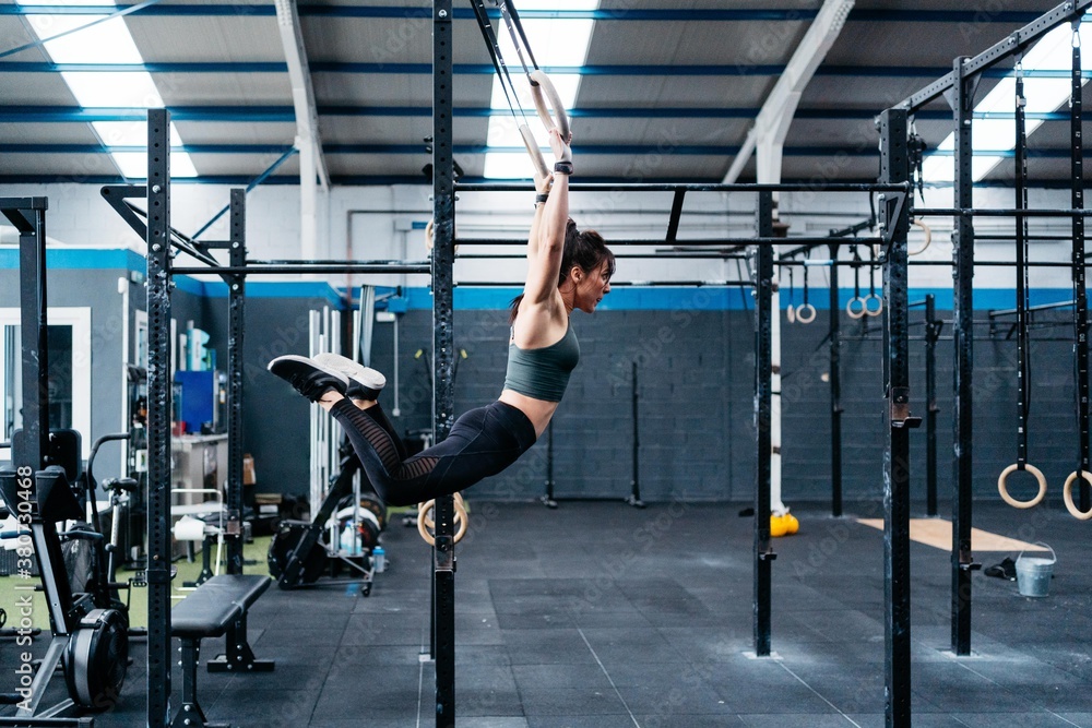 Side view of a woman athlete hanging from rings during a crossfit training Side view of a woman athlete hanging from rings during a crossfit training