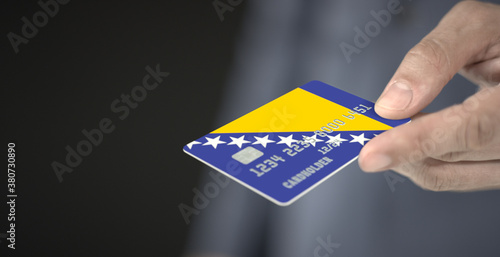 Man gives credit card with printed flag of Bosnia and Herzegovina. Fictional numbers