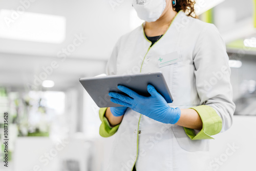 Unrecognizable female pharmacist using tablet wearing gloves and face mask photo