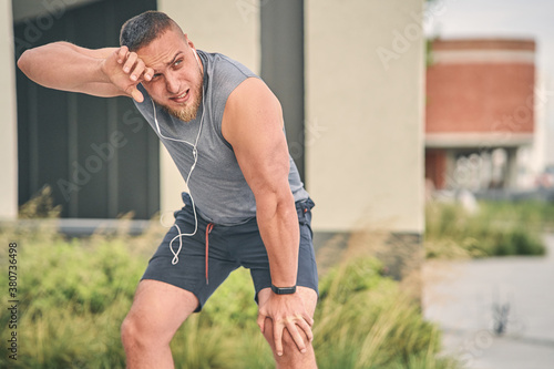 A bodybuilder in sportswear with headphones in his ears stopped to rest during a day jog. Sport concept