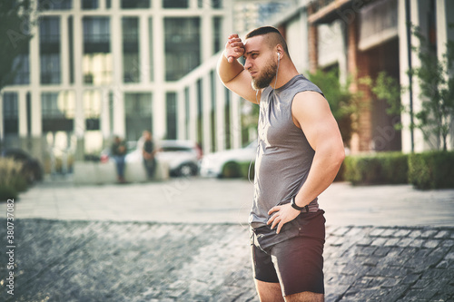 A muscular man  in sportswear with headphones in his ears stopped to rest during a jog. Sport concept © IC Production