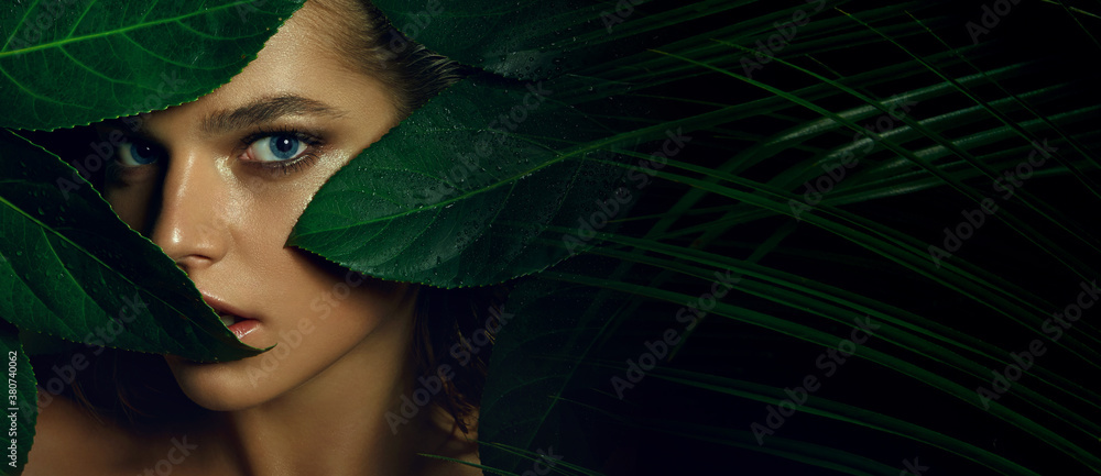 A beautiful tanned young woman with natural makeup and wet hair stands in the jungle among exotic plants. Tropical plants, nature. - obrazy, fototapety, plakaty 