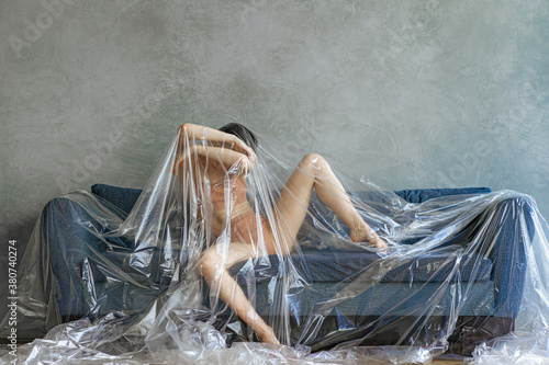 concept photo. The girl is lying under a cellophane film on the sofa