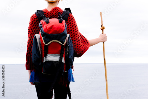 Cropped back view of unrecognizable female hiker with trekking stick standing against gray cloudy sky and enjoying freedom during pilgrimage through Spain