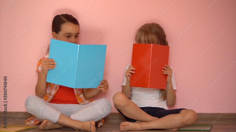 Little girls reading a book in living room. Smart schoolgirls doing their homework after school. Education and distance learning for kids. Homeschooling during quarantine. Stay at home entertainment. Little girls reading a book in living room. Smart schoolgirls doing their homework after school. Education and distance learning for kids. Homeschooling during quarantine. Stay at home entertainment.