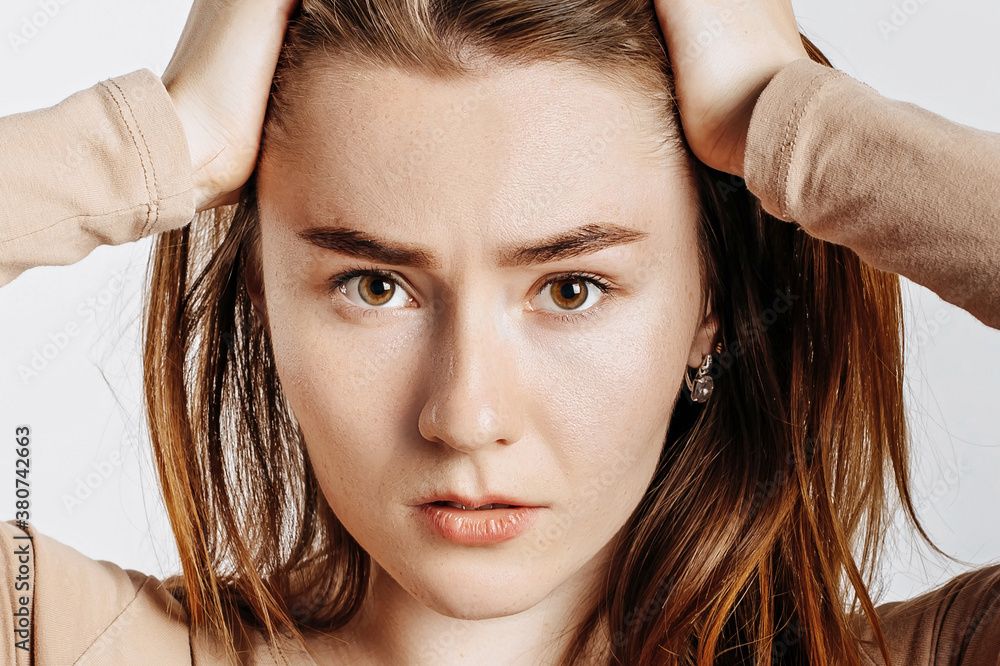 Naklejka premium Beautiful young brunette girl in horror holding her head on an isolated white background. The woman is shocked by the bad news. Advertising space