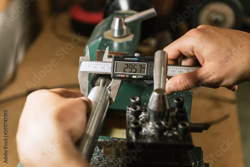 Unrecognizable technician standing at workbench and using caliper for precise gauging while working in shabby workshop photo
