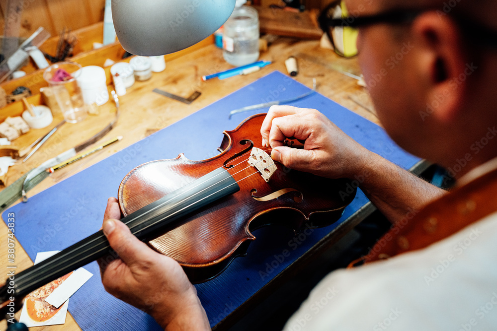 Crop male artisan master setting bridge on violin after replacing