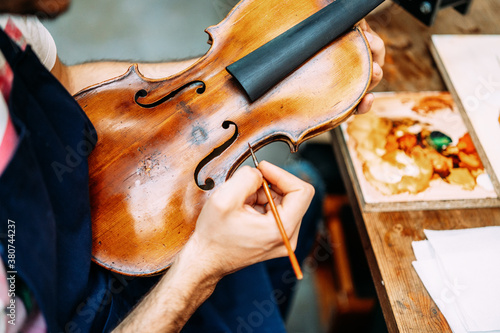 Side view of crop anonymous craftsman painting antique violin during restoration work in workshop