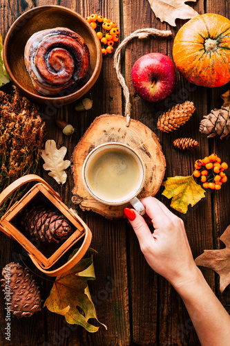 Autumn comfort. Cappuccino in hand and cinnabon rolls. Pumpkins and dry leaves on a wooden background. Rustic style. © yakovlevadaria
