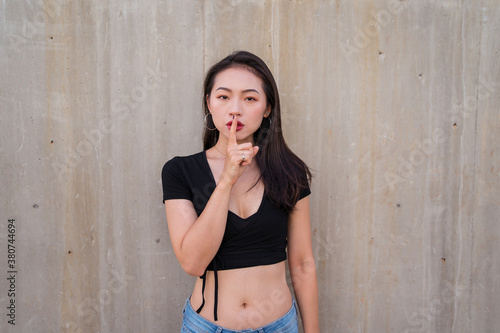 Calm Asian female standing with index finger on lips and demonstrating hush sign while looking at camera