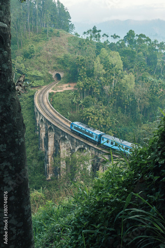 From above of blue train running on aged Nine Arch Bridge located amidst green hills in Sri Lanka photo